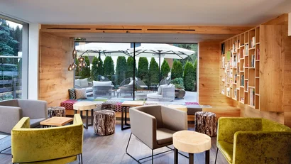 Moderner Sitzbereich mit Holzmöbeln und Bücherregal vor Terrasse mit Sonnenschirmen