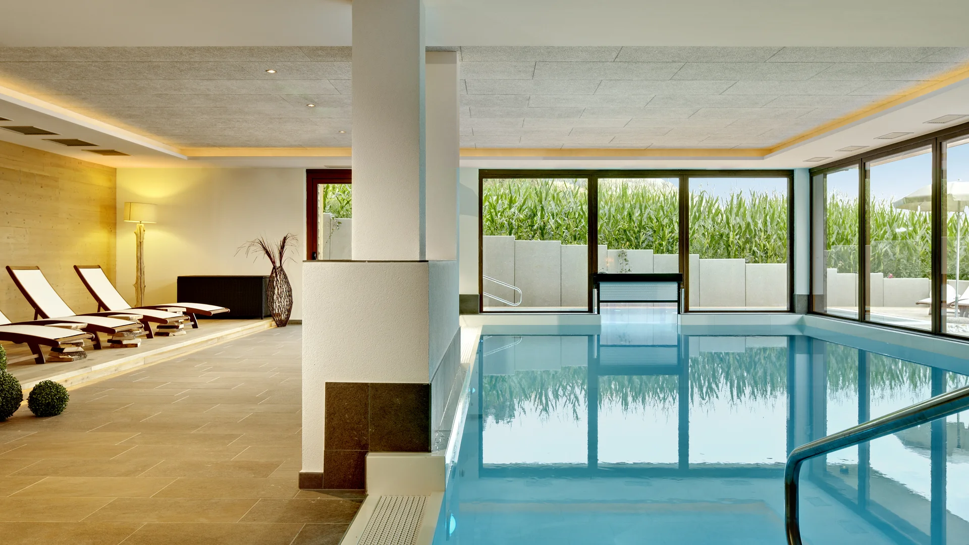 Piscina interna moderna con sedie a sdraio e grandi finestre verso l'esterno