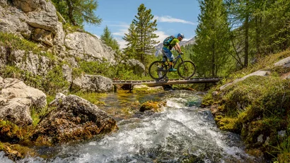 Mountainbiker fährt auf schmaler Brücke über Gebirgsbach