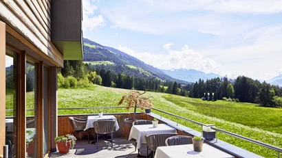 Terrasse mit Tischen und Stühlen bietet Aussicht auf grüne Wiesen und Berge