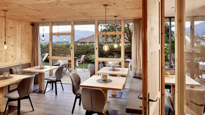 Gemütlicher Gastraum mit Holzmöbeln und Blick auf die Terrasse und Berge