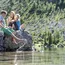 Drei Kinder sitzen am Ufer eines klaren Bergsees und plantschen im Wasser