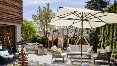 Gemütliche Terrasse mit Sitzmöbeln, Sonnenschirm und Spielplatz im Garten