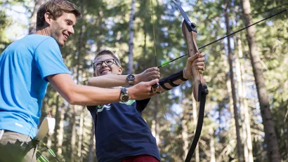 Junger Mann hilft Jungen beim Bogenschießen im Wald