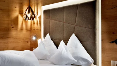 Modernes Bett mit vier weißen Kissen und hölzernem Kopfteil und Wandleuchte