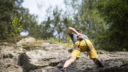 Mann klettert an einer Felswand mit Kletterausrüstung